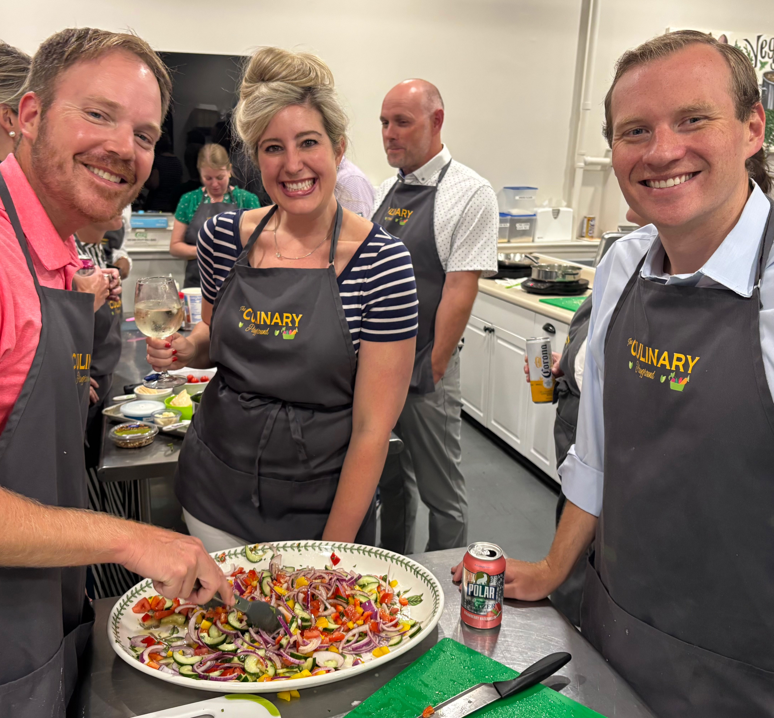 Two men and a woman smiling while mixing vegetables together during a cooking class.