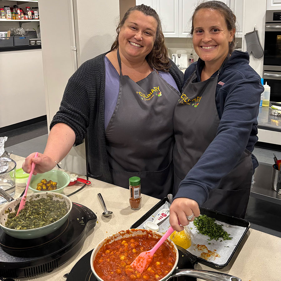 Two women smiling while posing with food being cooked