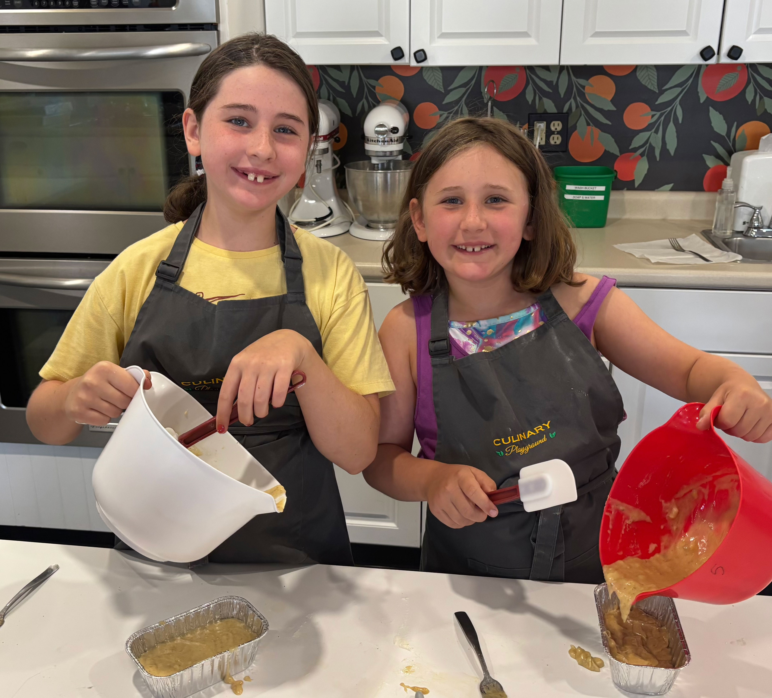 Two girls smiling while mixing bread dough during a baking class.