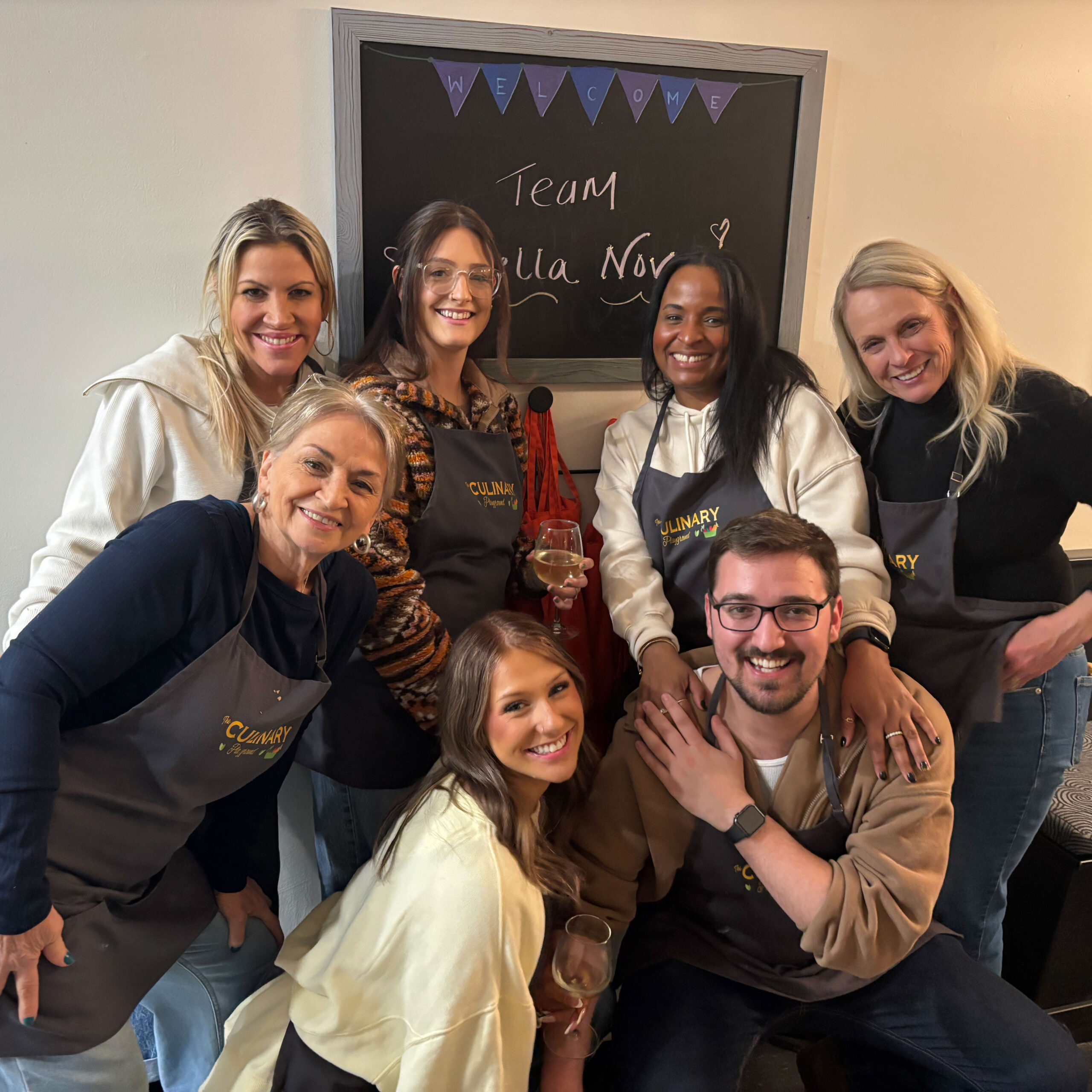 Group of people smiling and posing in front of a team board