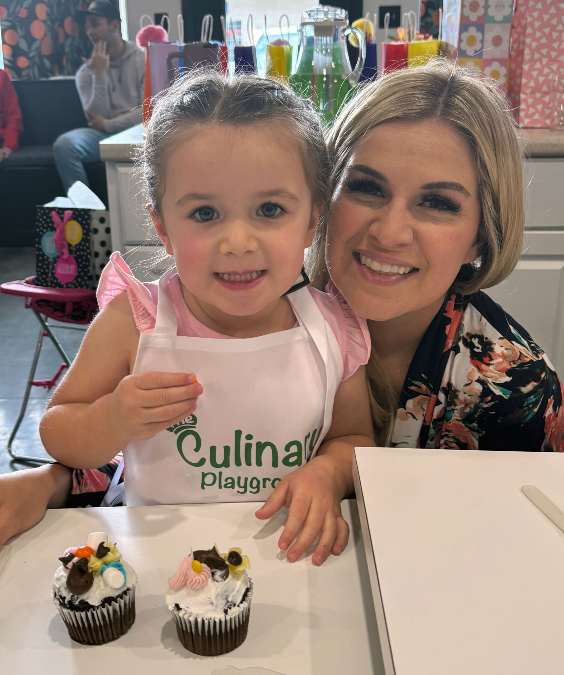 Mom and daughter smiling in front of birthday cupcakes